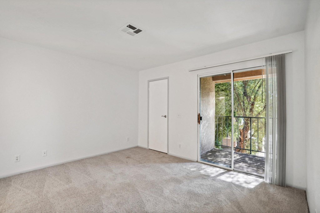 A room with a carpeted floor and a sliding glass door leading to a balcony.