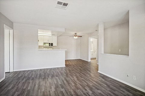 the living room and kitchen of an apartment with white walls and wood flooring