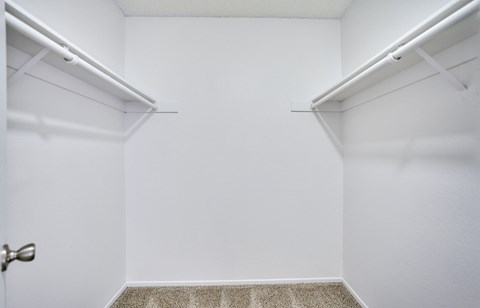 A white room with a carpeted floor and two white shelves on the wall.