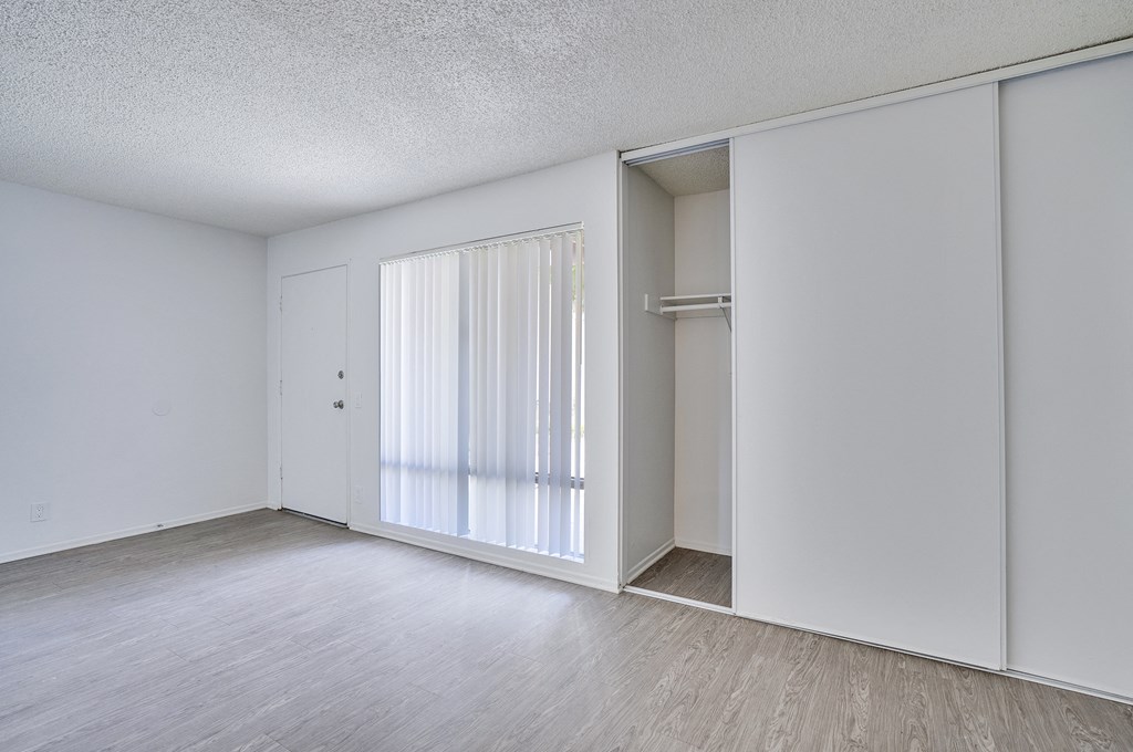 A room with a white door, a window with white curtains, and a white closet.