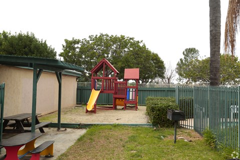A playground with a red slide and a red and white playhouse.