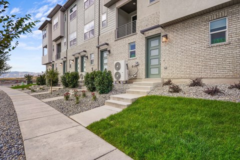 a sidewalk in front of an apartment building with grass and plants