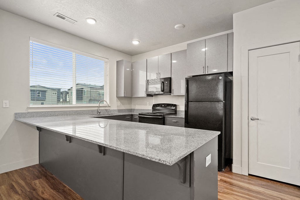 A kitchen with a black refrigerator and a granite countertop.