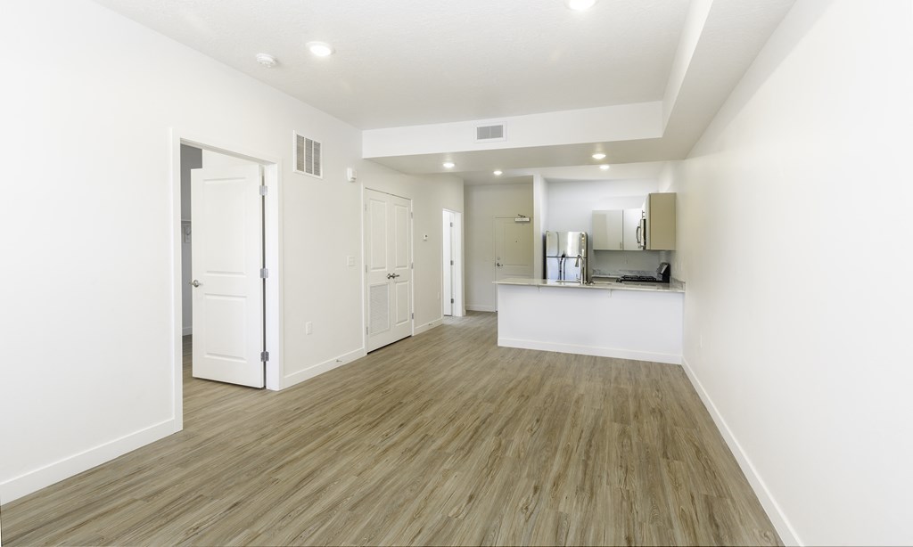 a living room and kitchen with white walls and wood floors