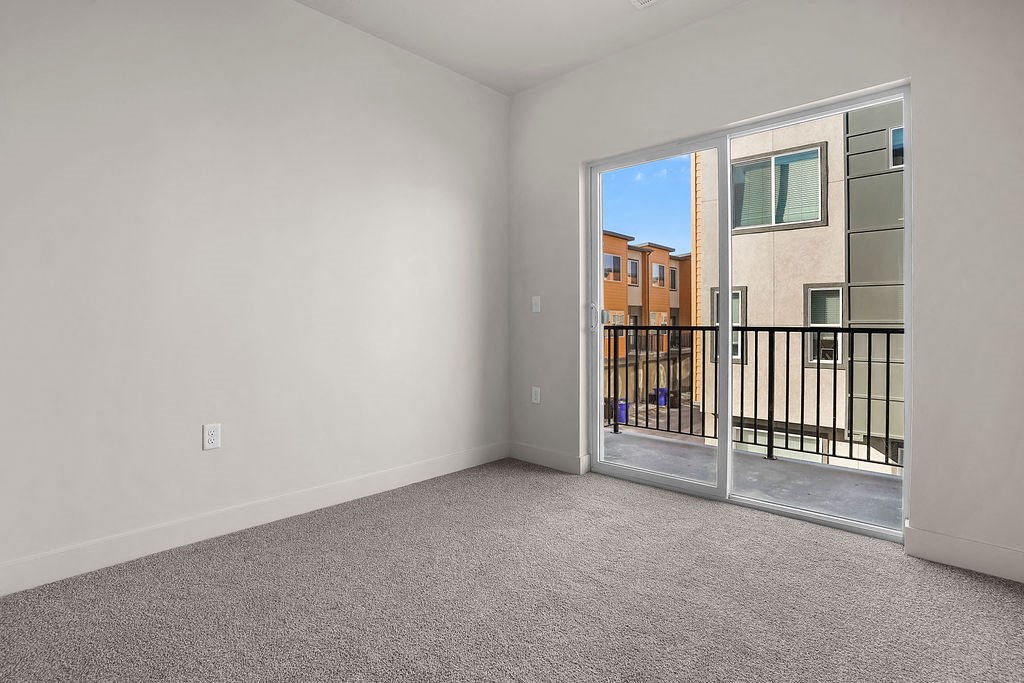 A room with a carpeted floor and a sliding glass door leading to a balcony.