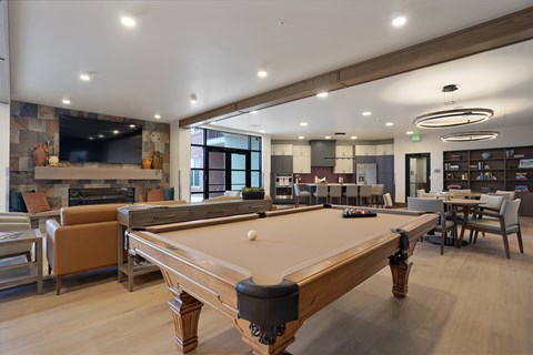 A pool table is in the middle of a room with a bar and a TV.