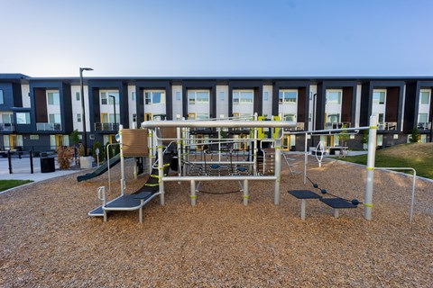 A playground with a slide, swings, and a bench in front of a building.