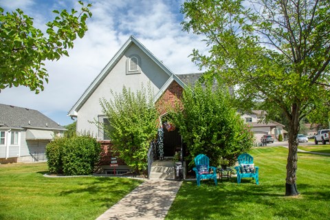A white house with a red brick chimney and a small porch with blue chairs.