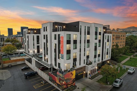 A modern building with a mural on the side is surrounded by a parking lot.