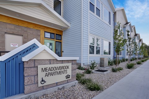 A sign for Meadowbrook Apartments is displayed in front of a building.