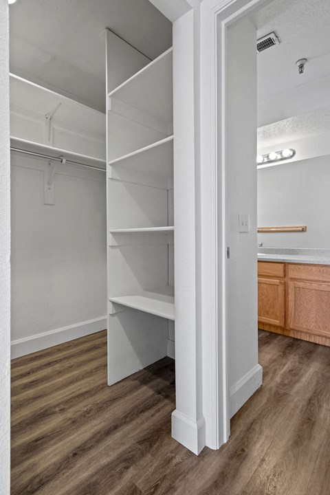 A white closet with shelves and a doorway leading to a kitchen.