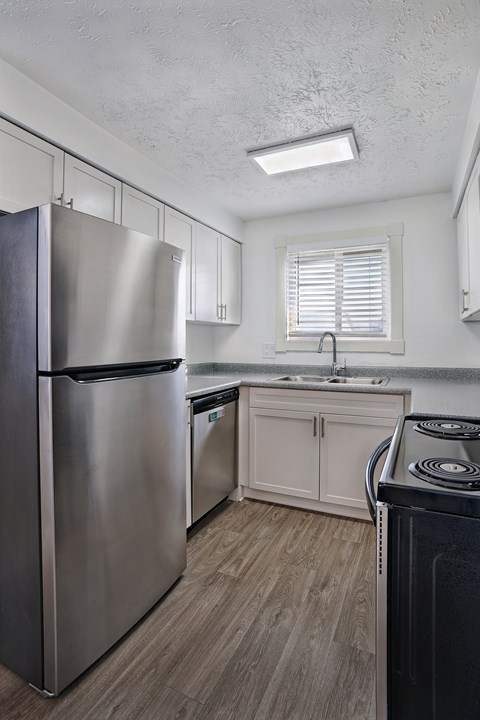 A modern kitchen with a stainless steel refrigerator and wooden flooring.