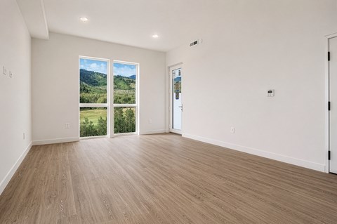 A room with wooden flooring and a view of the outdoors through the windows.