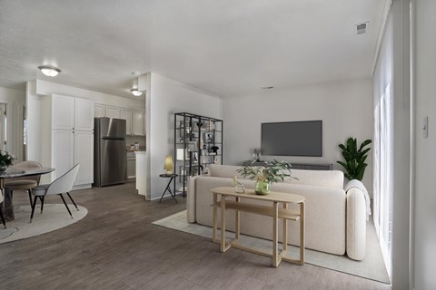 A modern living room with a white sofa, a wooden coffee table, and a TV on the wall.