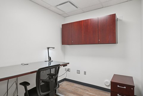 A white desk with a black chair and a white table top with a black base and a black lamp on it.