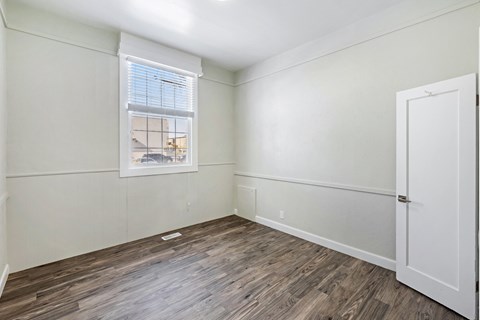 a bedroom with white walls and wood flooring and a window