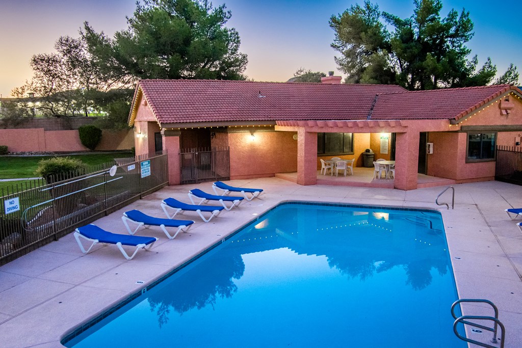 a swimming pool in front of a house with blue chairs