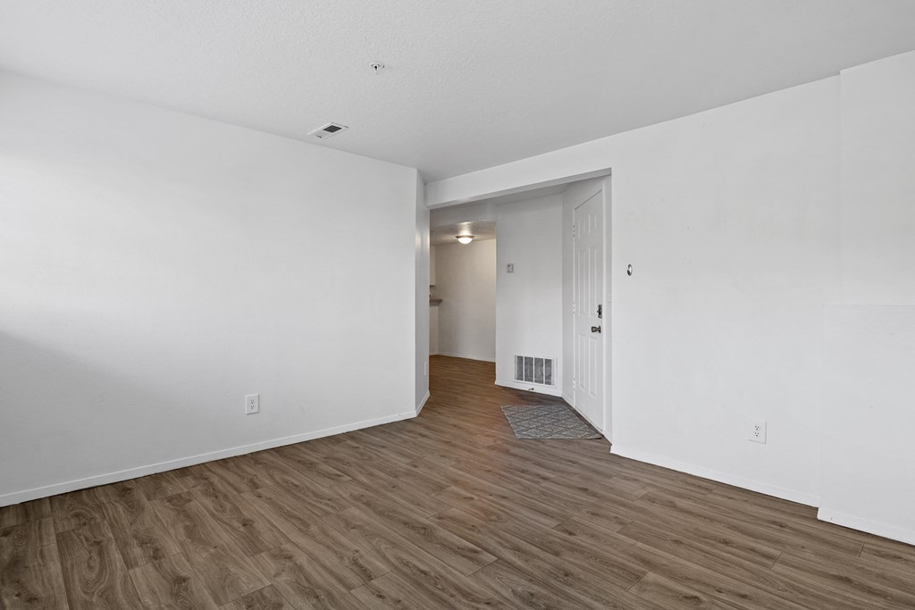 the living room of an apartment with white walls and wood flooring