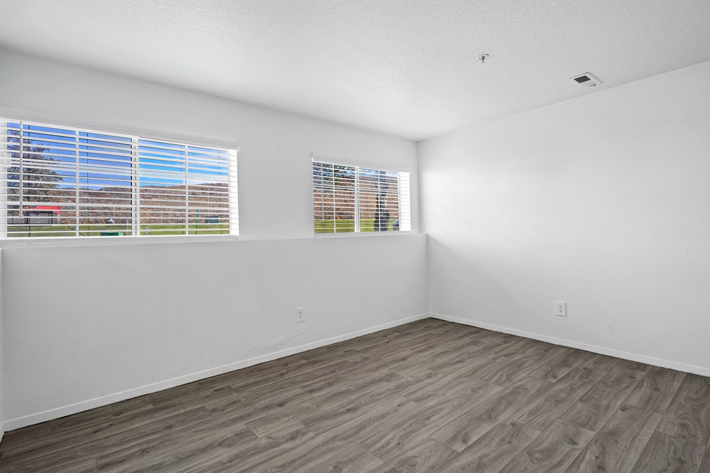 the living room of an apartment with wood flooring and two windows