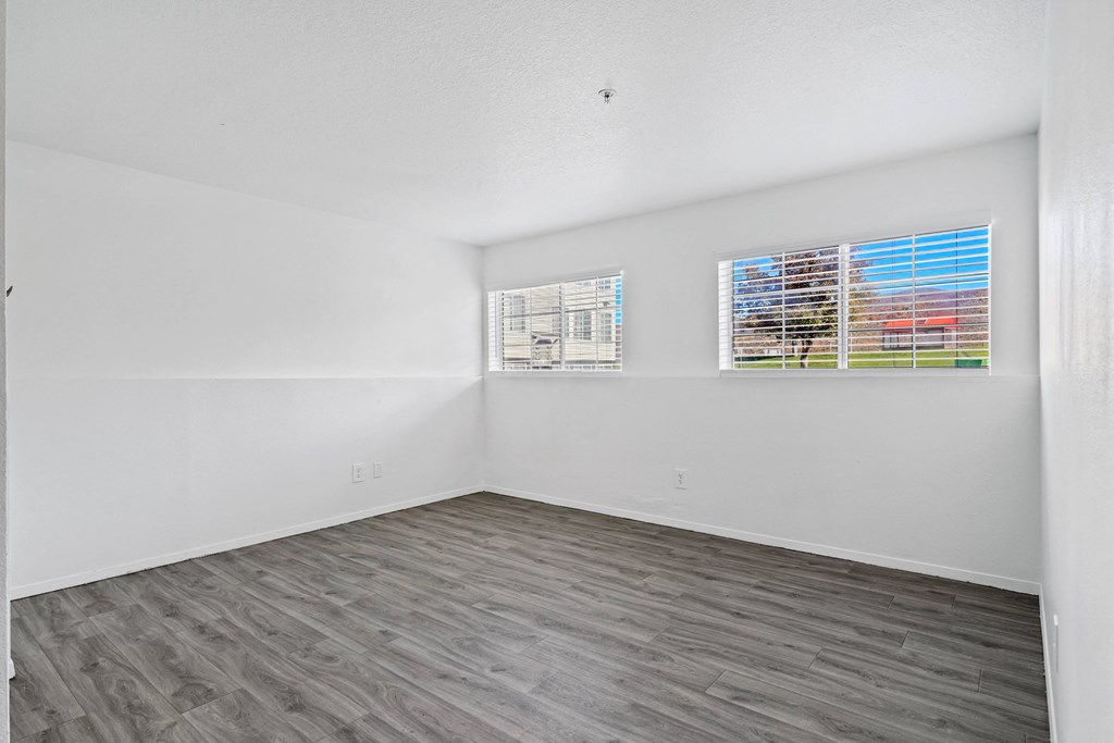an empty room with white walls and wood flooring and two windows