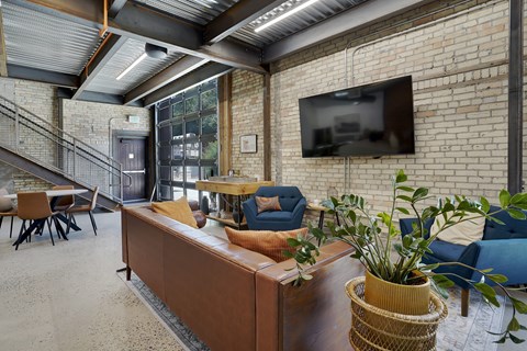 A living room with a couch, chairs, and a television mounted on a brick wall.