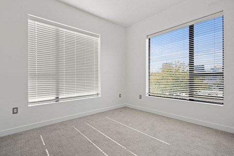 an empty room with two windows with blinds and