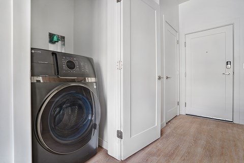 A washing machine is in a small room with a door on the right.