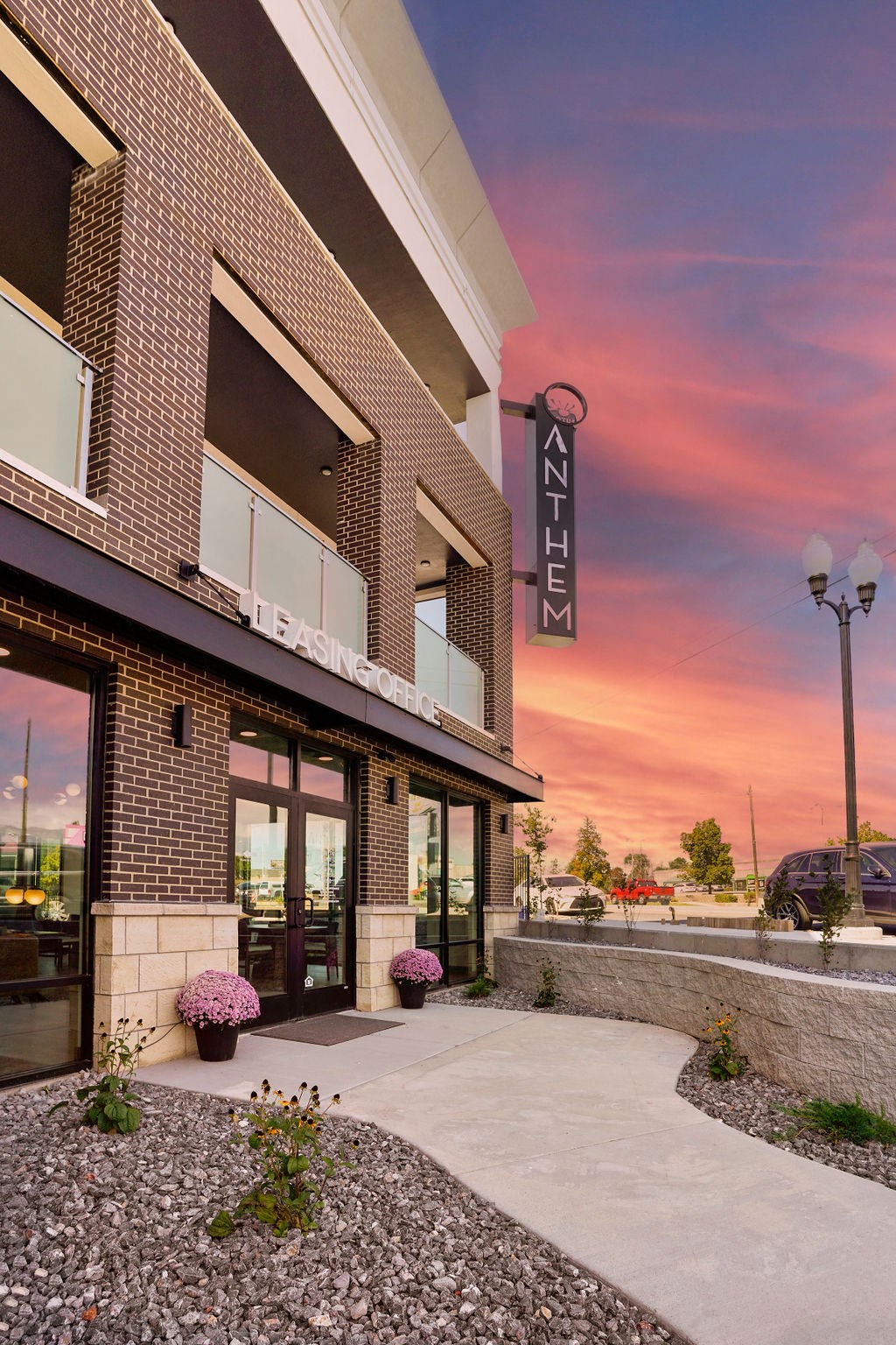 a walkway leading to the entrance of a brick building with a pink sunset in the background