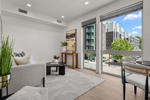 A living room with a grey couch, a coffee table, and a large window with a view of the street.