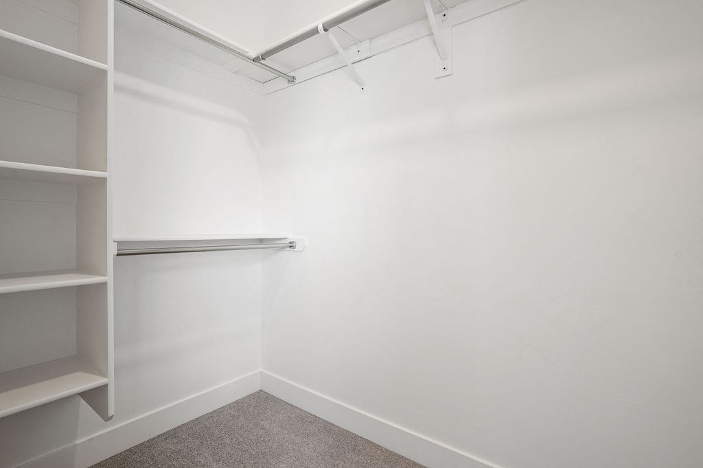 a walk in closet in a white room with shelves