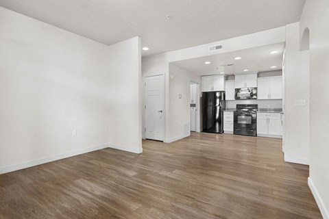 A kitchen with white cabinets and a black fridge is visible from a living room.