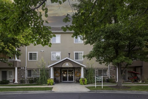 A building with a brown facade and a white door is surrounded by greenery.