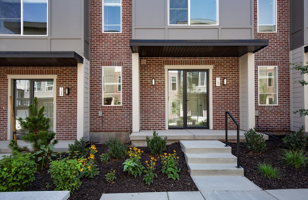 Front of a building with stairs and plants at Greens by Lotus Townhomes, Ogden, 84403