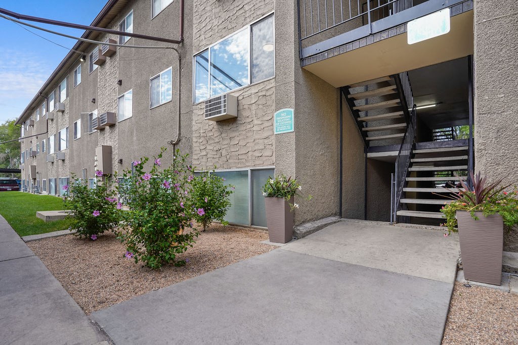 the entrance to an apartment building with a concrete walkway and flowers