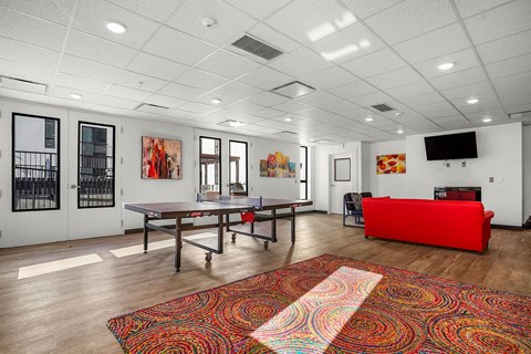 A room with a red couch and a table with a red cushion.