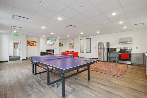 A ping pong table is in the middle of a room with a kitchen area in the background.