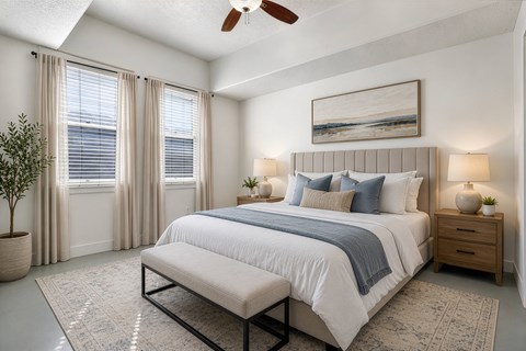 A bedroom with a large bed, a ceiling fan, and a painting on the wall.