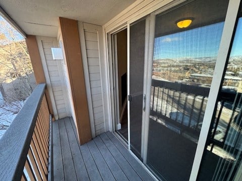 A balcony with a glass door leading to a view of a cityscape.