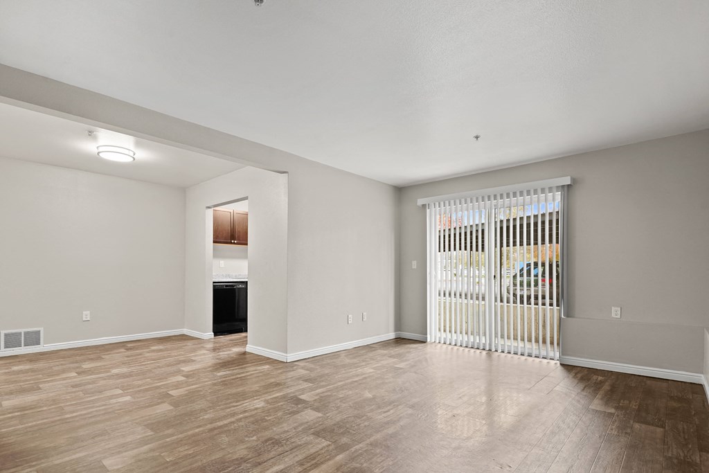 an empty living room with a sliding glass door to a kitchen