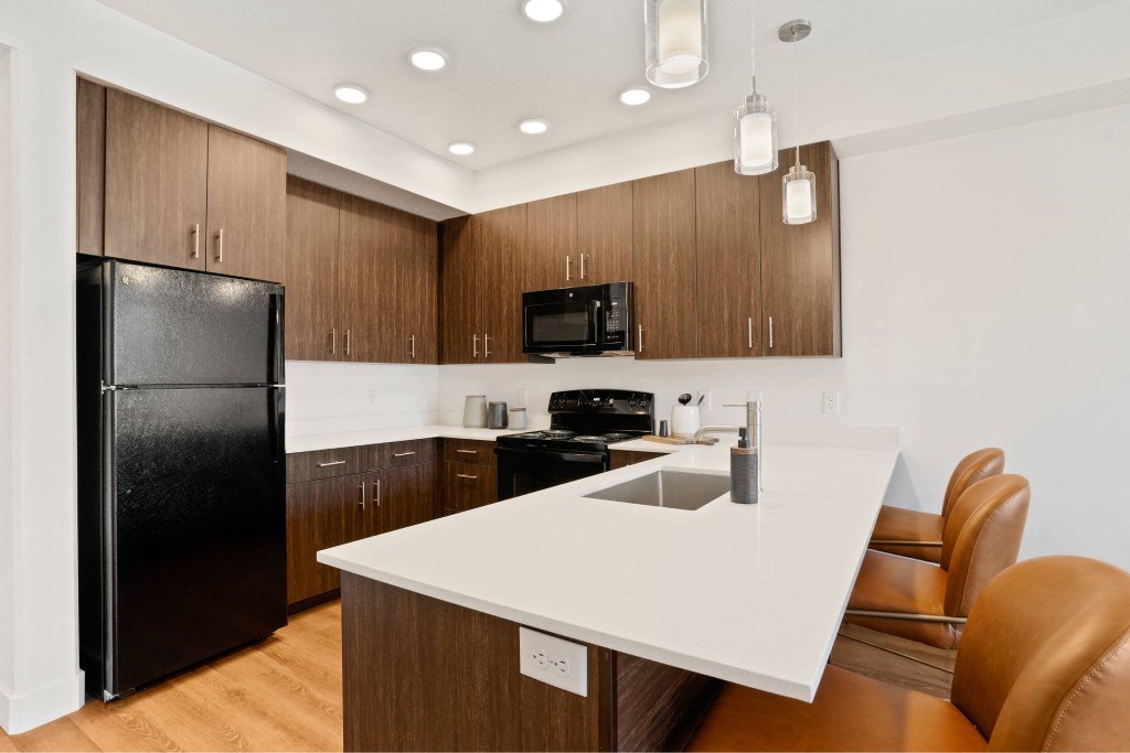 A modern kitchen with a black fridge, white countertops, and brown cabinets.