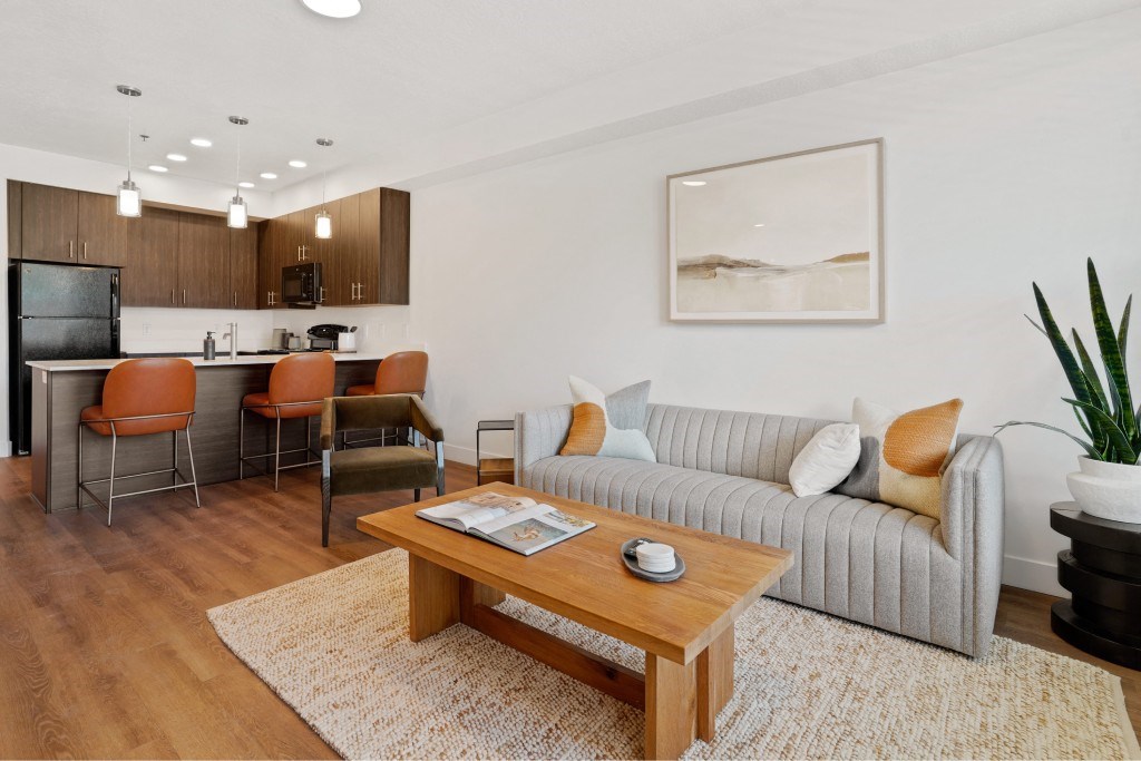 A living room with a grey couch, a wooden coffee table, and a kitchen area in the background.