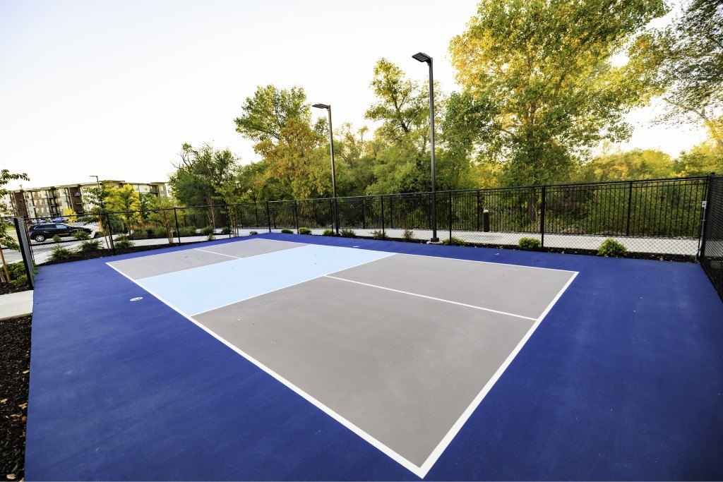 A blue tennis court surrounded by a black fence.