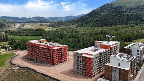 A large building with a red and orange exterior is surrounded by smaller buildings and greenery.
