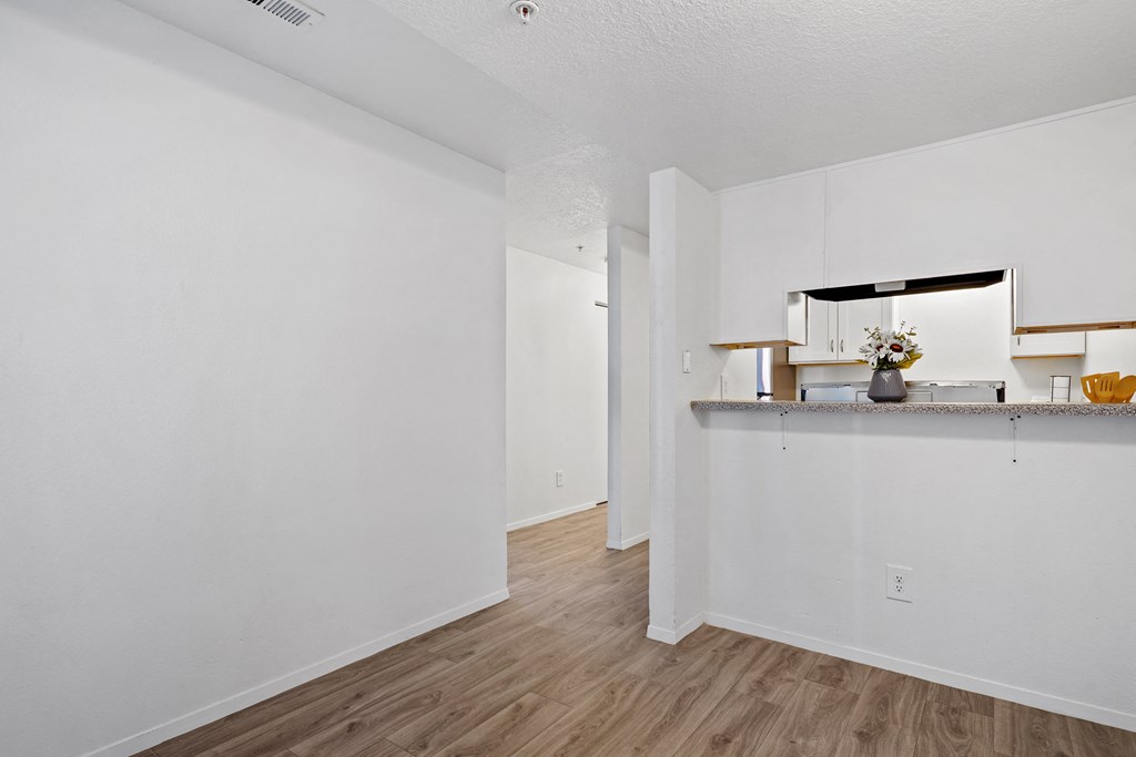 the living room and kitchen of an apartment with white walls and wood flooring