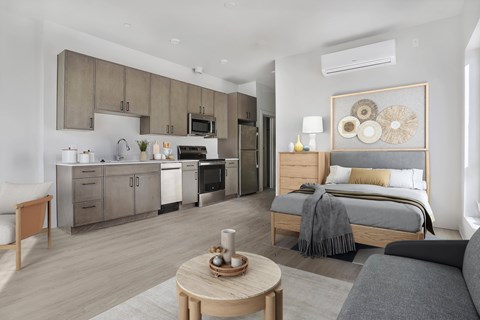 A modern bedroom with a large bed and a kitchen area in the background.