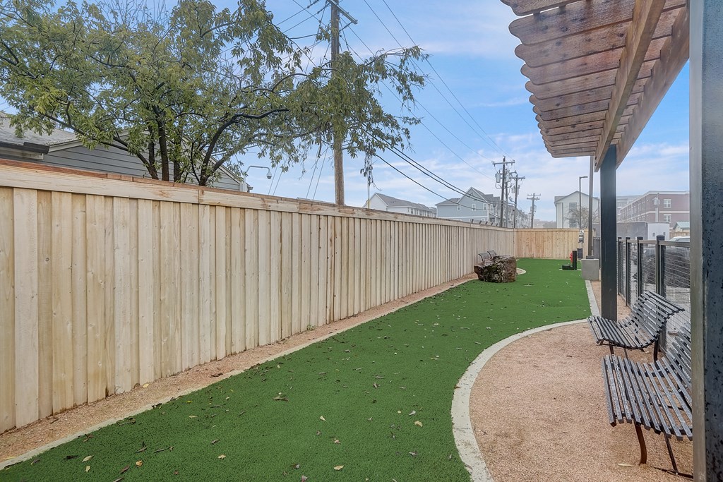 the backyard has a fenced in area with artificial grass and benches
