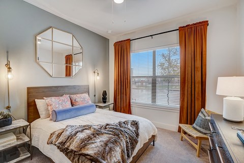Bedroom with wooden bed frame and large mirror at The Mill Old Town Apartments, Lewisville, TX