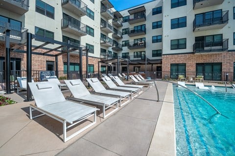 A pool area with sun loungers and apartment buildings in the background.