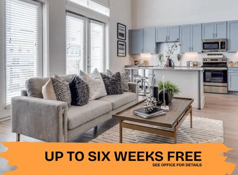A modern living room with a grey sofa and a coffee table in front of a kitchen.