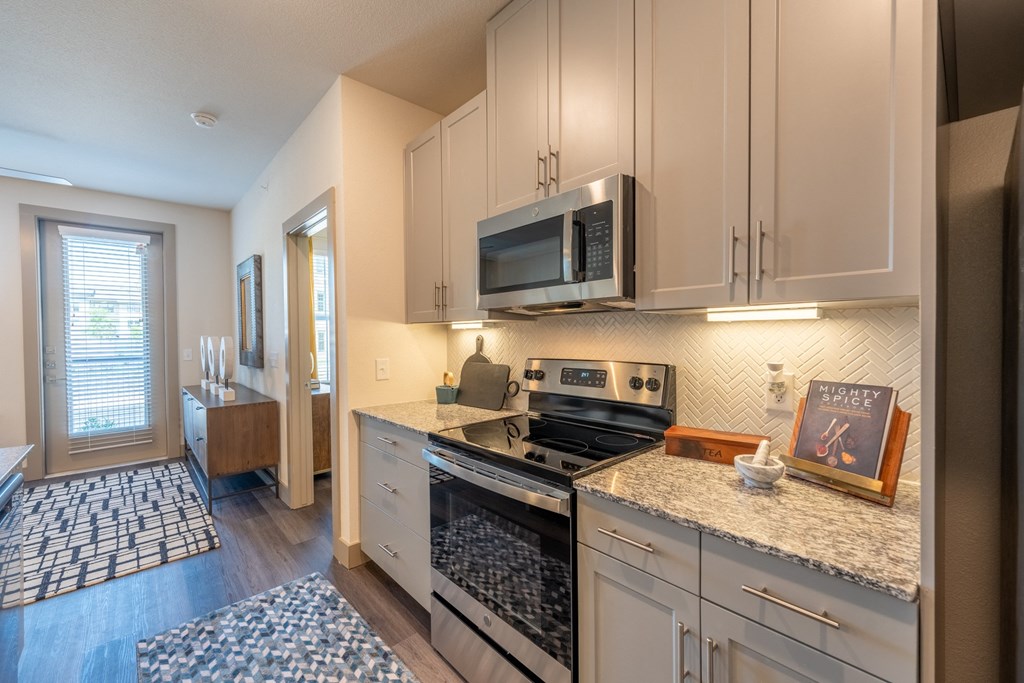 a kitchen with white cabinets and granite countertops at One Preston Station, Celina, 75009
